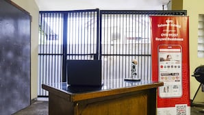 A reception desk with a laptop, a poster advertising OYO Selamat Datang, and a view of a gated area.