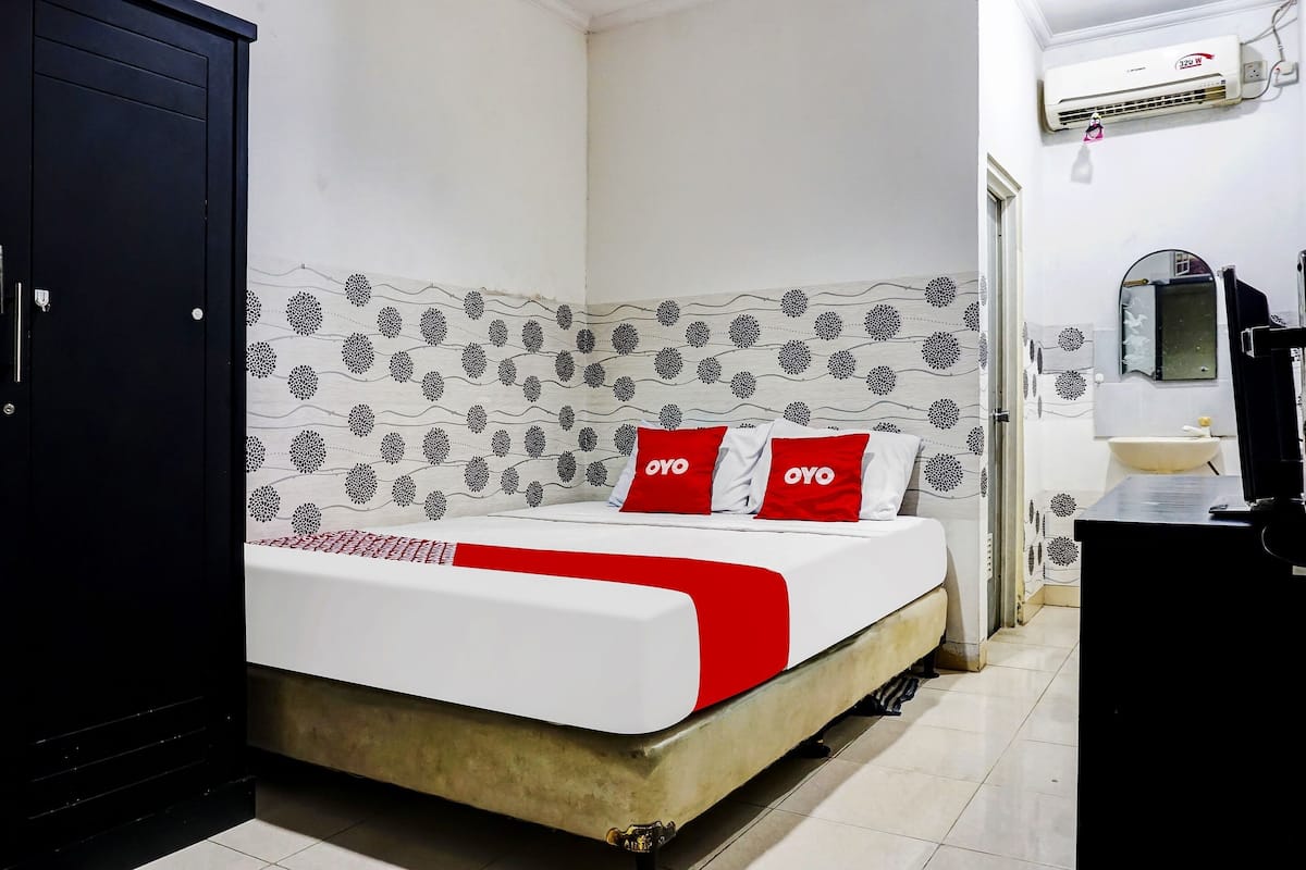 Una cama con una colcha blanca y roja, dos almohadas con la marca 'OYO', un armario negro, un lavamanos blanco y un espejo.