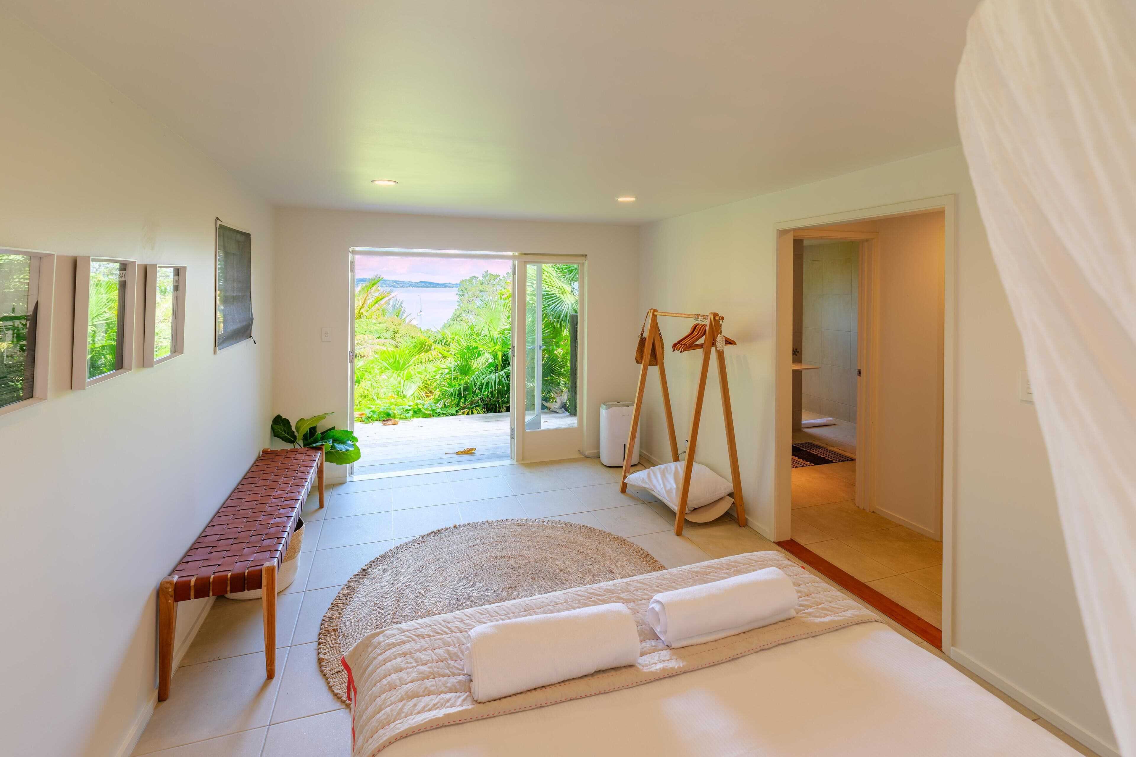 A bedroom with a bed, a bench, a swing, and a view of greenery.