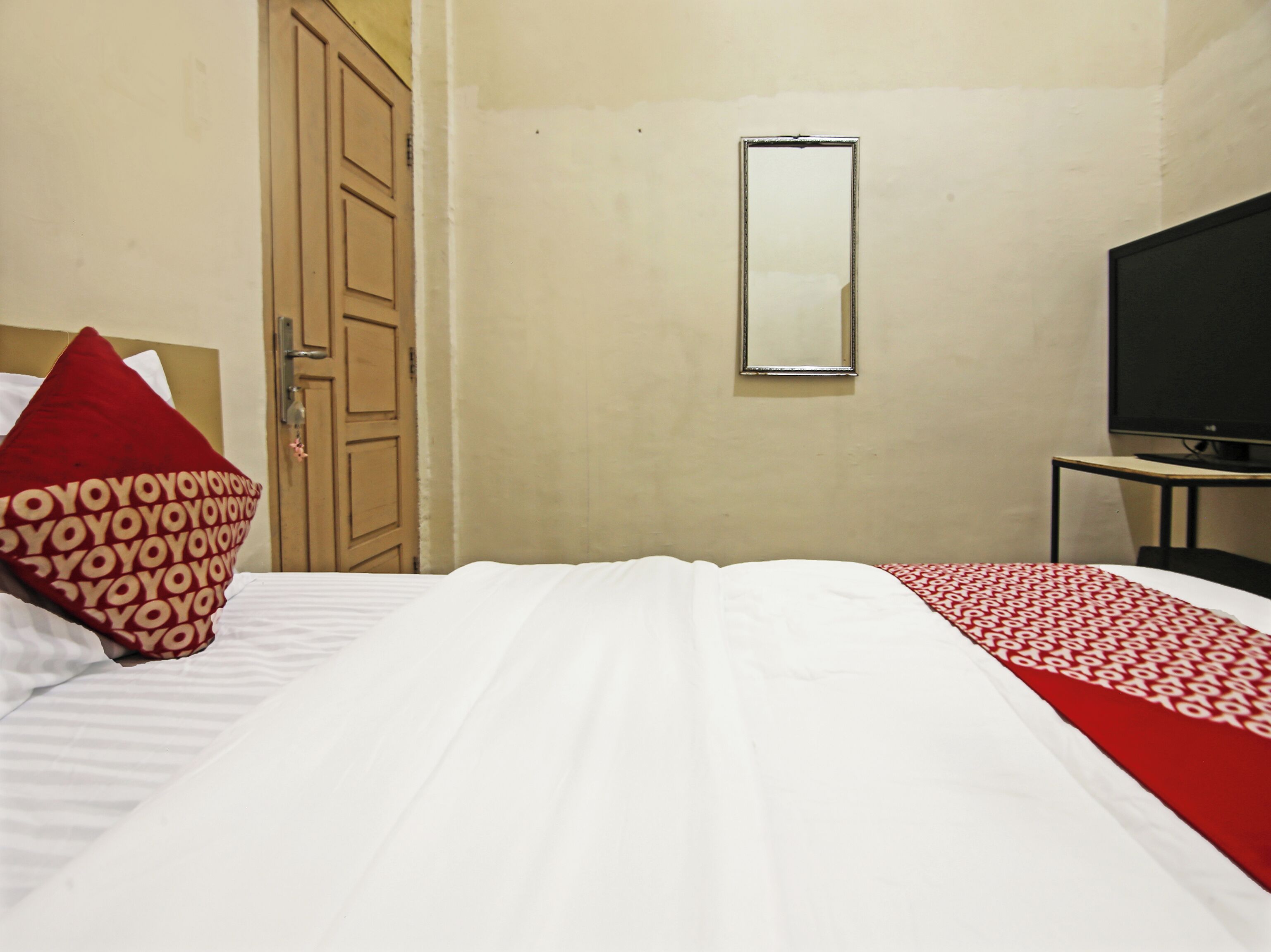 Una habitación de hotel con cama, televisión, espejo y puerta.