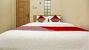 A single bed with white bedding and red accents, a wooden door, and a window with decorative glass. - OYO Life 91268 Homestay Bu Erma Syariah (Palembang)