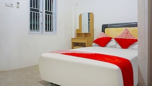 A bedroom with a bed, a bedside table, a mirror, and a window.