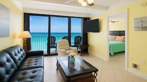 Ein Zimmer mit einer schwarzen Ledersofa, einem Couchtisch, einem Deckenventilator und einem großen Fenster mit Blick auf das Meer.