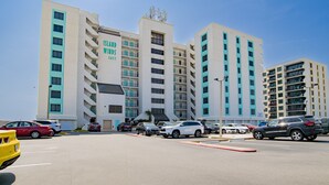 Ein mehrstöckiges Hotel mit modernem Design, mit Balkonen in jeder Etage und einem Parkplatz davor.