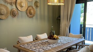 Een eethoek met een houten tafel, rieten stoelen en een hanglamp.