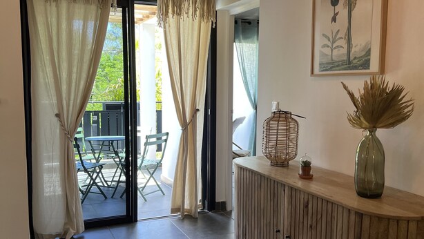 Een modern interieur met een houten receptiebalie, een plantenkunstwerk in een lijst en uitzicht op een terras.