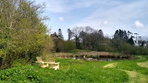 Un cadre extérieur paisible avec une pelouse, un étang et deux chaises en bois.