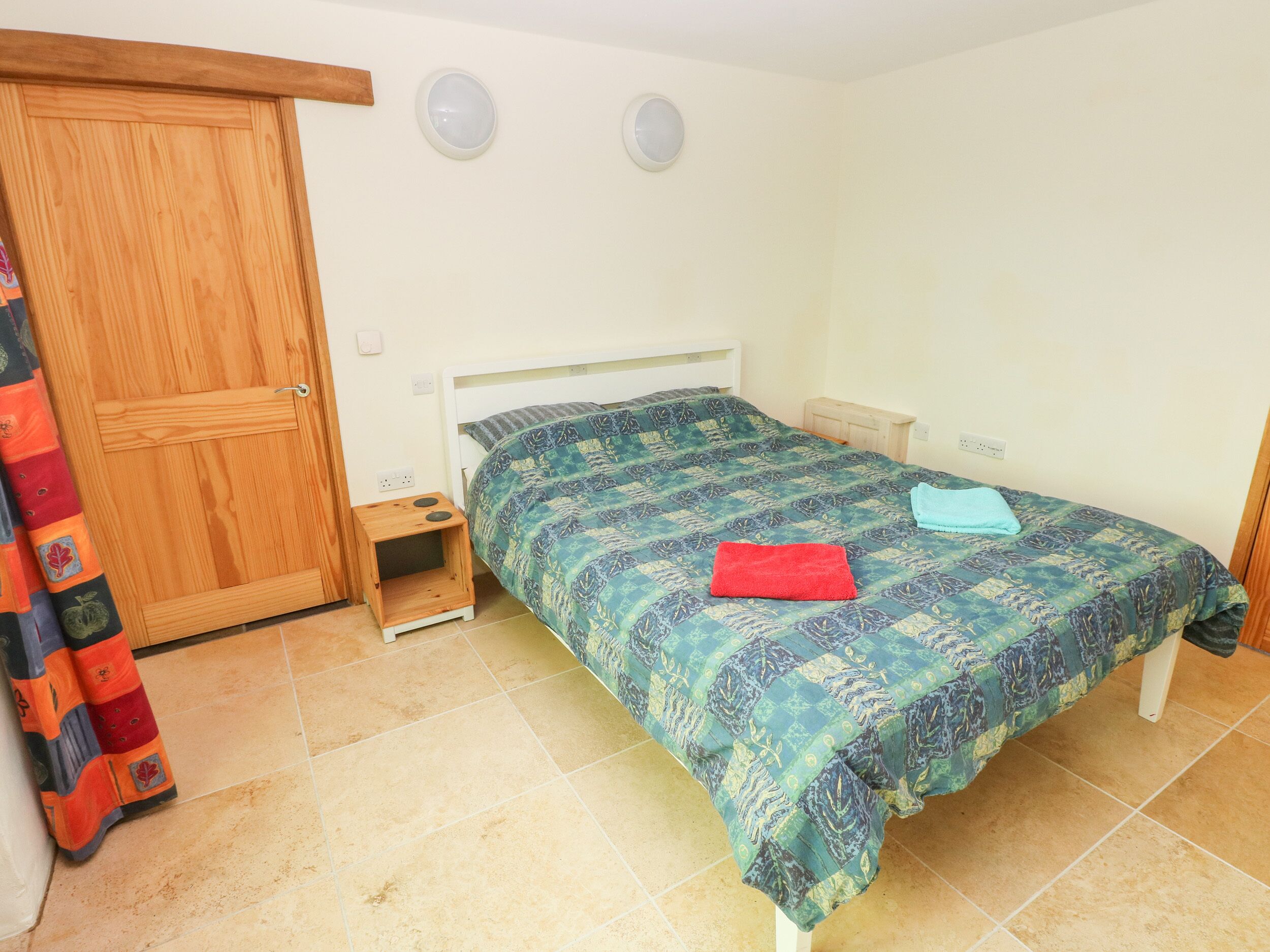 A bedroom with a bed, a wooden wardrobe, a small bedside table, and a curtain.