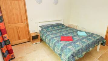 A bedroom with a bed, a wooden wardrobe, a small bedside table, and a curtain.