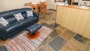 Un salon avec un canapé en cuir bleu, un tapis rayé aux couleurs vives et une table à manger en bois, accompagnée de chaises.