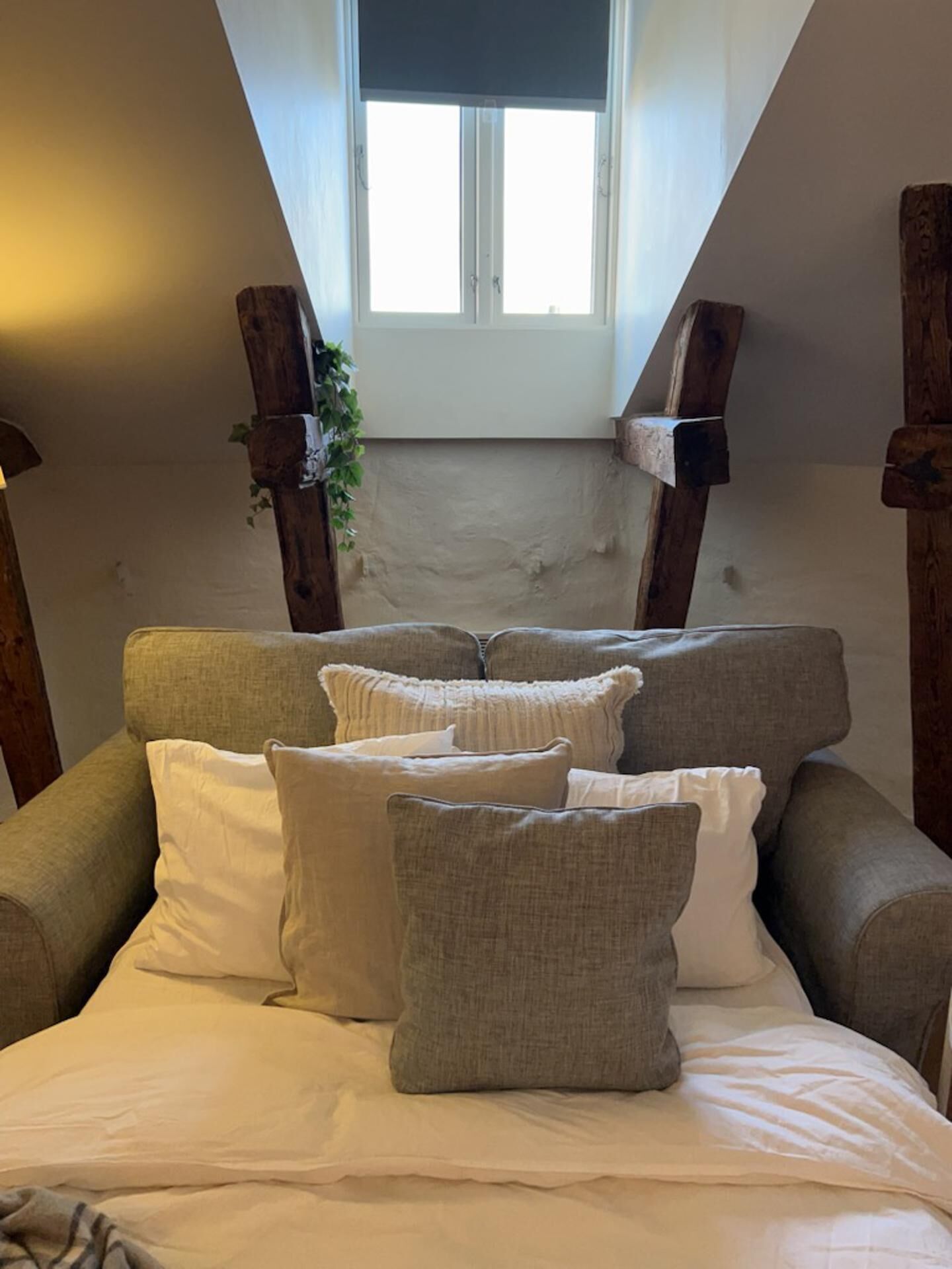 A cozy loft bedroom with a sloped ceiling, a large window, and a bed with multiple pillows.