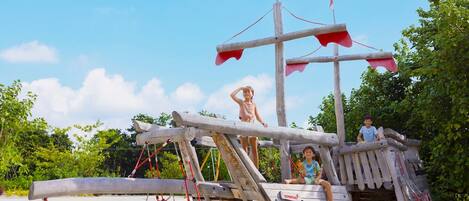 A wooden pirate ship play structure on a sandy beach with ropes and flags.