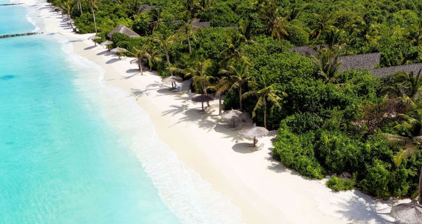 A beach resort with white sand, clear turquoise water, and lush green vegetation.