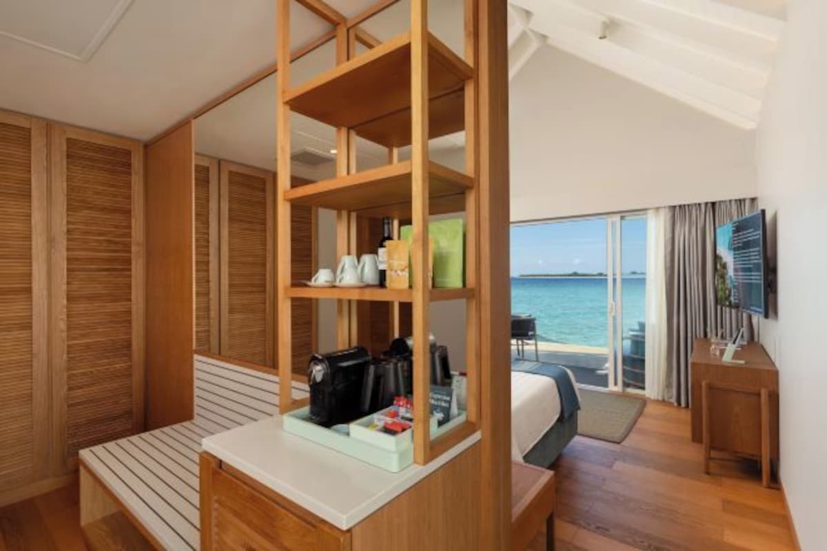 Una habitación de hotel con un ventanal grande, una estantería de madera, una cama y un televisor.