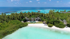 Vista aérea de un resort tropical con piscina privada, varias villas para huéspedes y una playa.