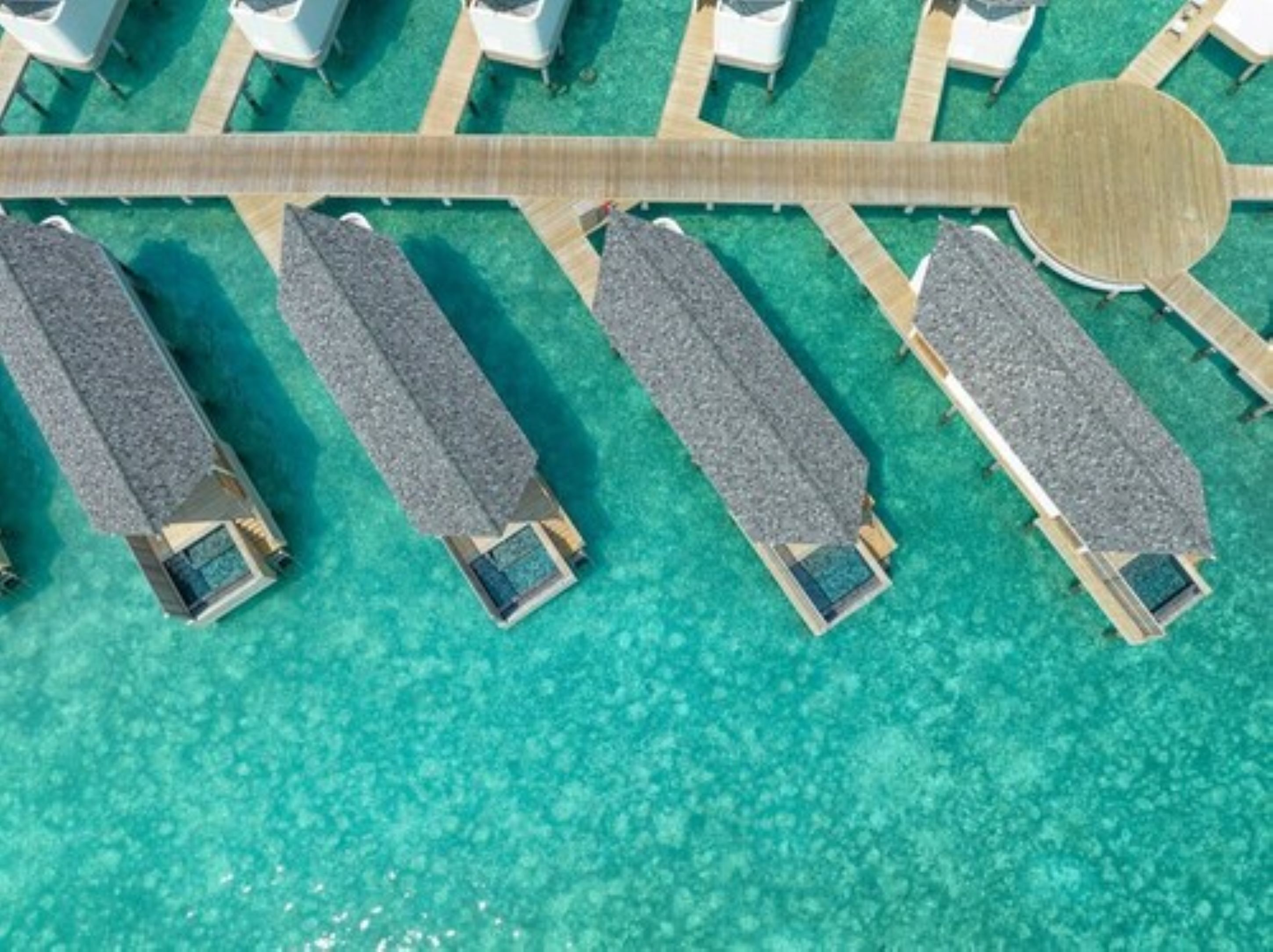 An aerial view of a resort with overwater bungalows connected by a wooden walkway.