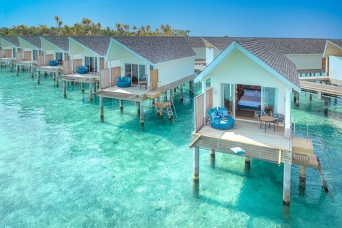 Bungalows über dem Wasser mit klarem türkisblauem Wasser, Holzterrasse und blau gepolsterten Sitzmöglichkeiten.
