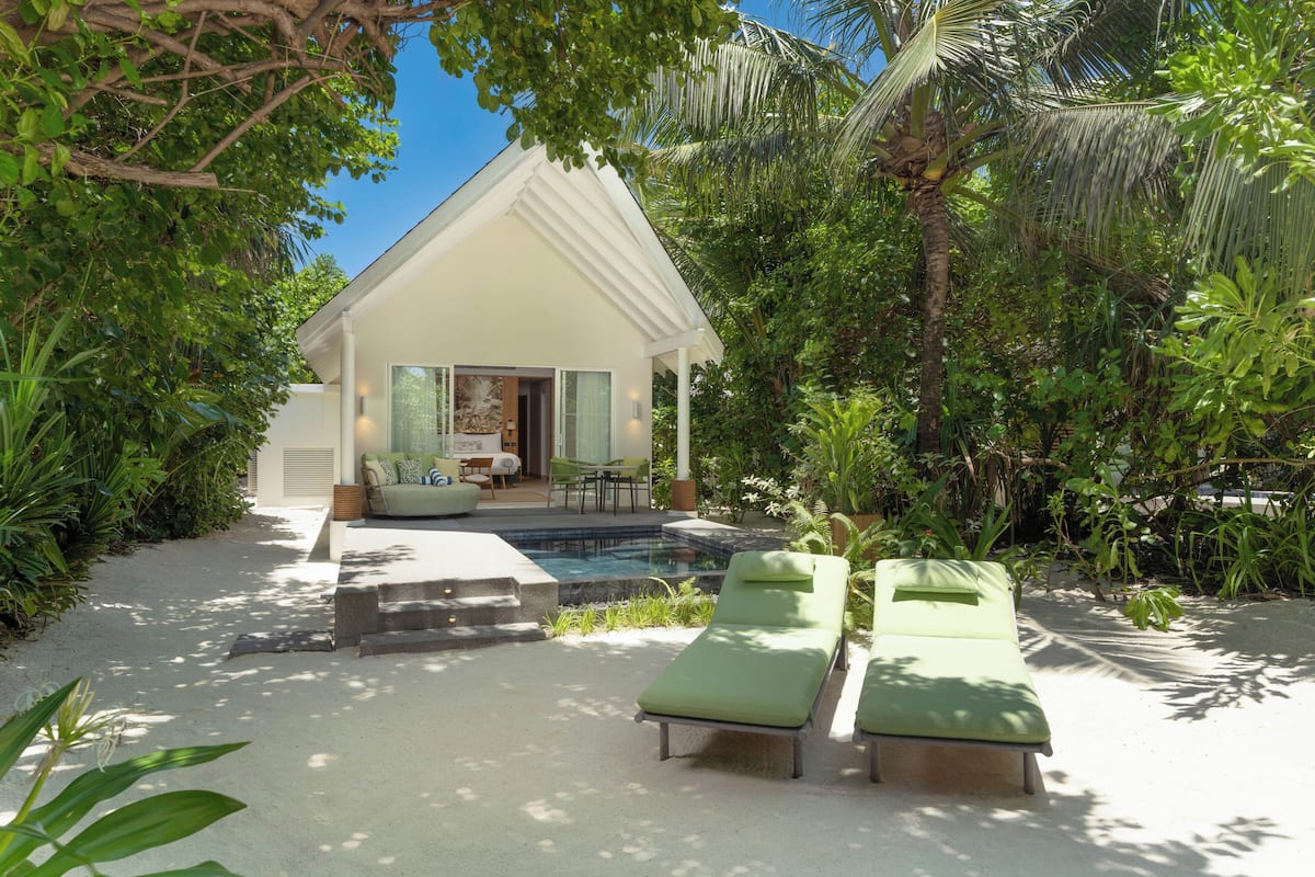 Eine moderne Villa mit Pool, zwei Liegestühlen und üppiger Bepflanzung.