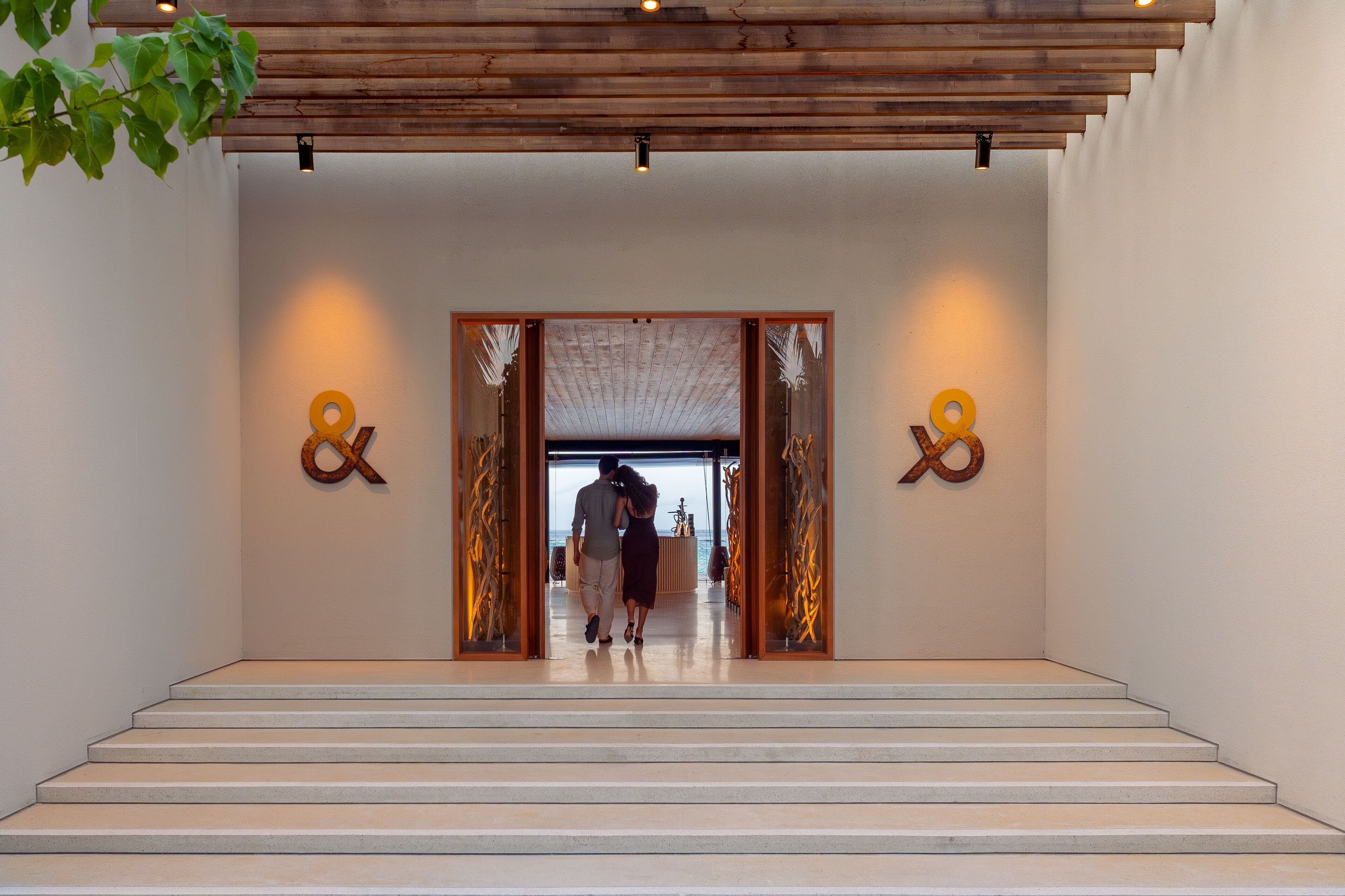 Une entrée d’hôtel moderne avec un plafond en bois, un escalier menant au hall d’entrée et des éléments décoratifs sur les murs.