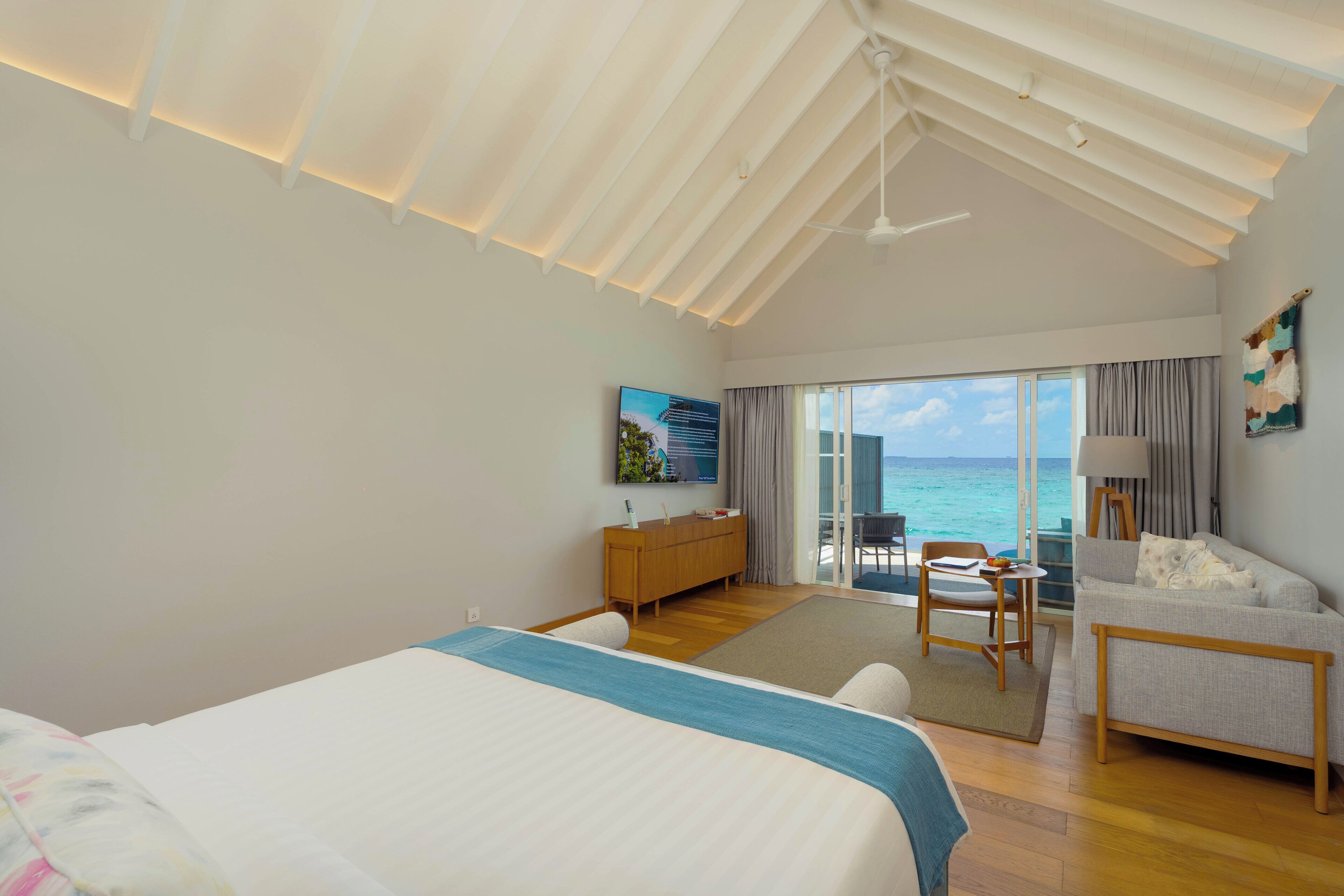 Un dormitorio amplio con una cama grande, un escritorio de madera, un sofá y un balcón con vista al océano.