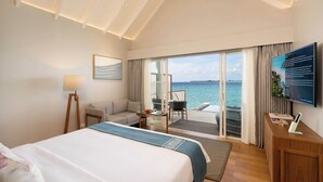 Habitación de hotel con cama, escritorio, silla, sofá, televisor y balcón con vista al mar.