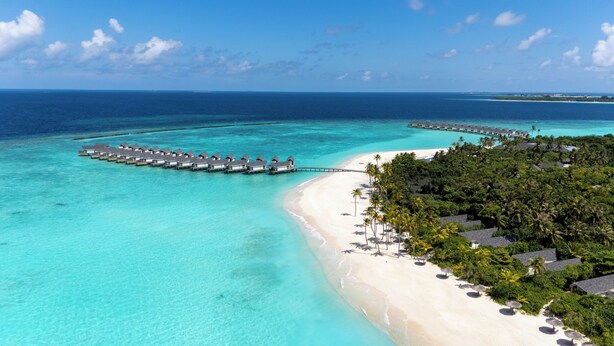 Zona de bungalows sobre el agua, con una playa y aguas turquesas cristalinas.