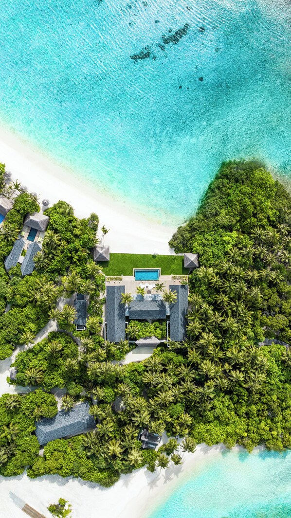 Ein Luftbild eines tropischen Resorts mit mehreren Villen, einem zentralen Pool und üppiger Vegetation.