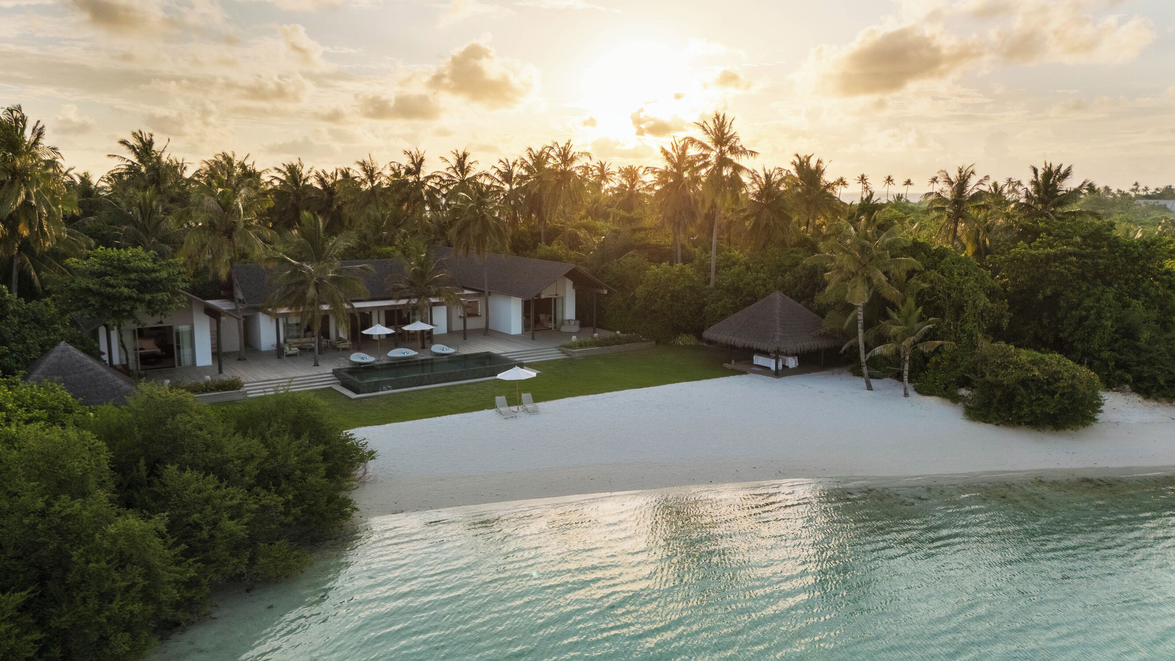 A beachfront property with a swimming pool, lounge chairs, and a thatched-roof hut.