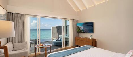 A hotel room with a large bed, a seating area with a view of the ocean, a television, and a wooden nightstand.