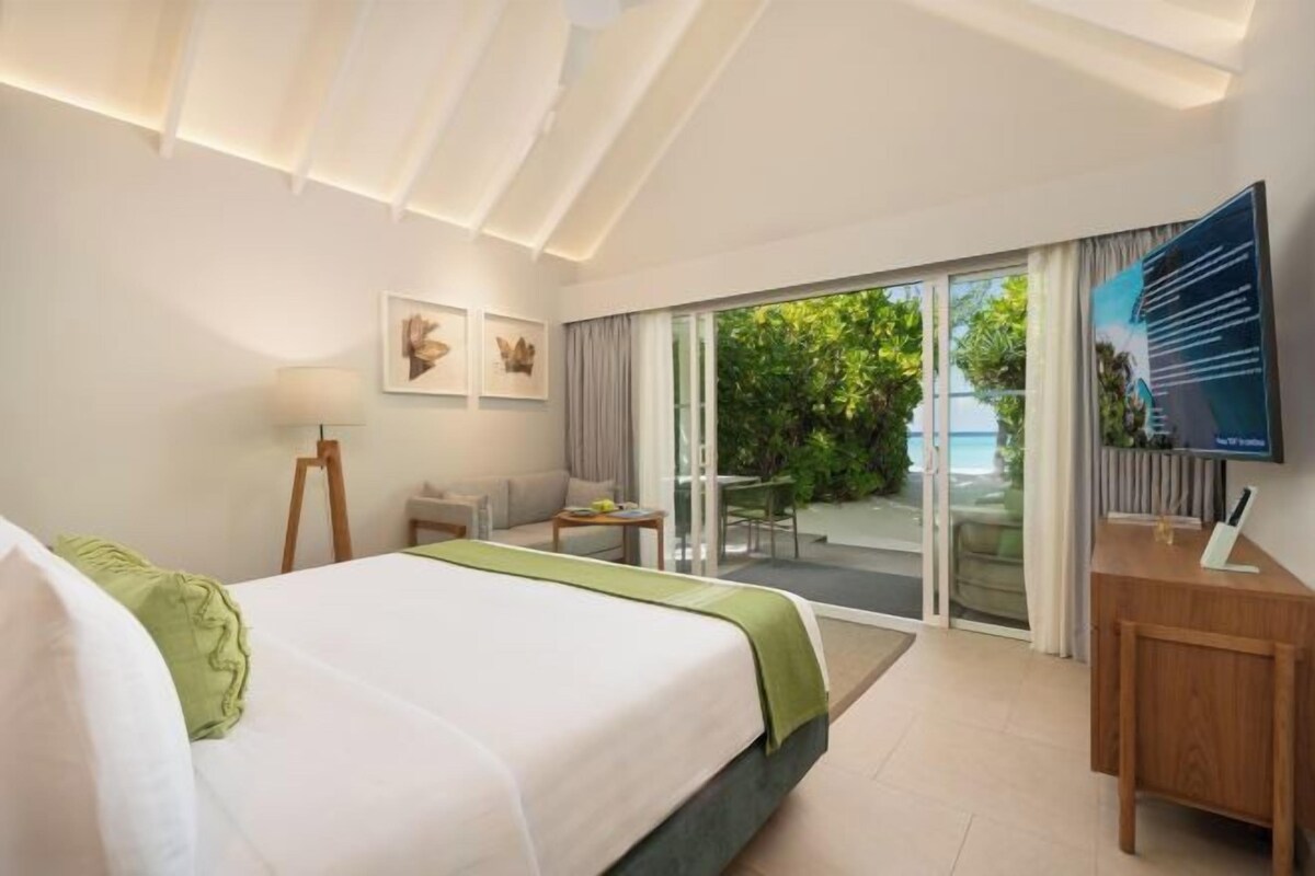 A hotel room with a bed, a desk, a chair, a television, and a sliding glass door leading to an outdoor area.