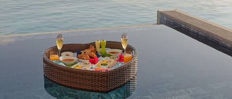 A floating dining table with a wicker basket containing food and drinks, overlooking a body of water.