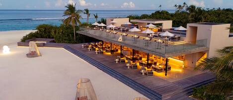 A beachfront resort with outdoor seating areas, a pool, and a view of the ocean.