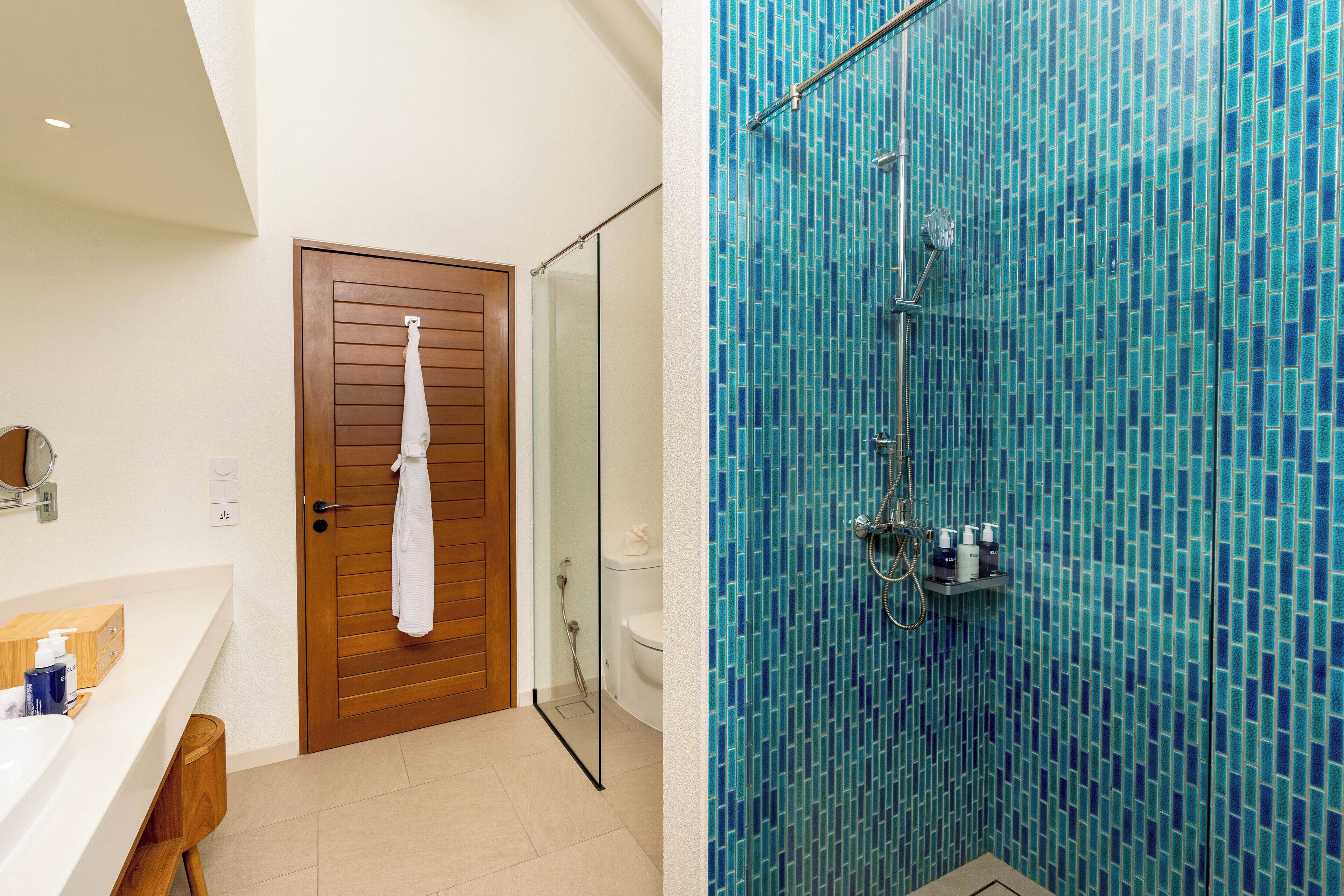 Un baño con puerta de madera, un lavabo blanco y una zona de ducha con azulejos azules.