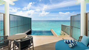 Una terraza de madera con piscina, sillones de descanso y vista al océano.