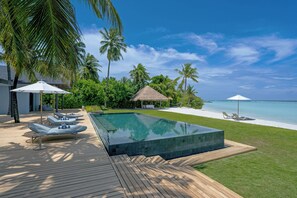 Ein Swimmingpool mit Liegestühlen, einer Holzterrasse und Blick auf den Strand.