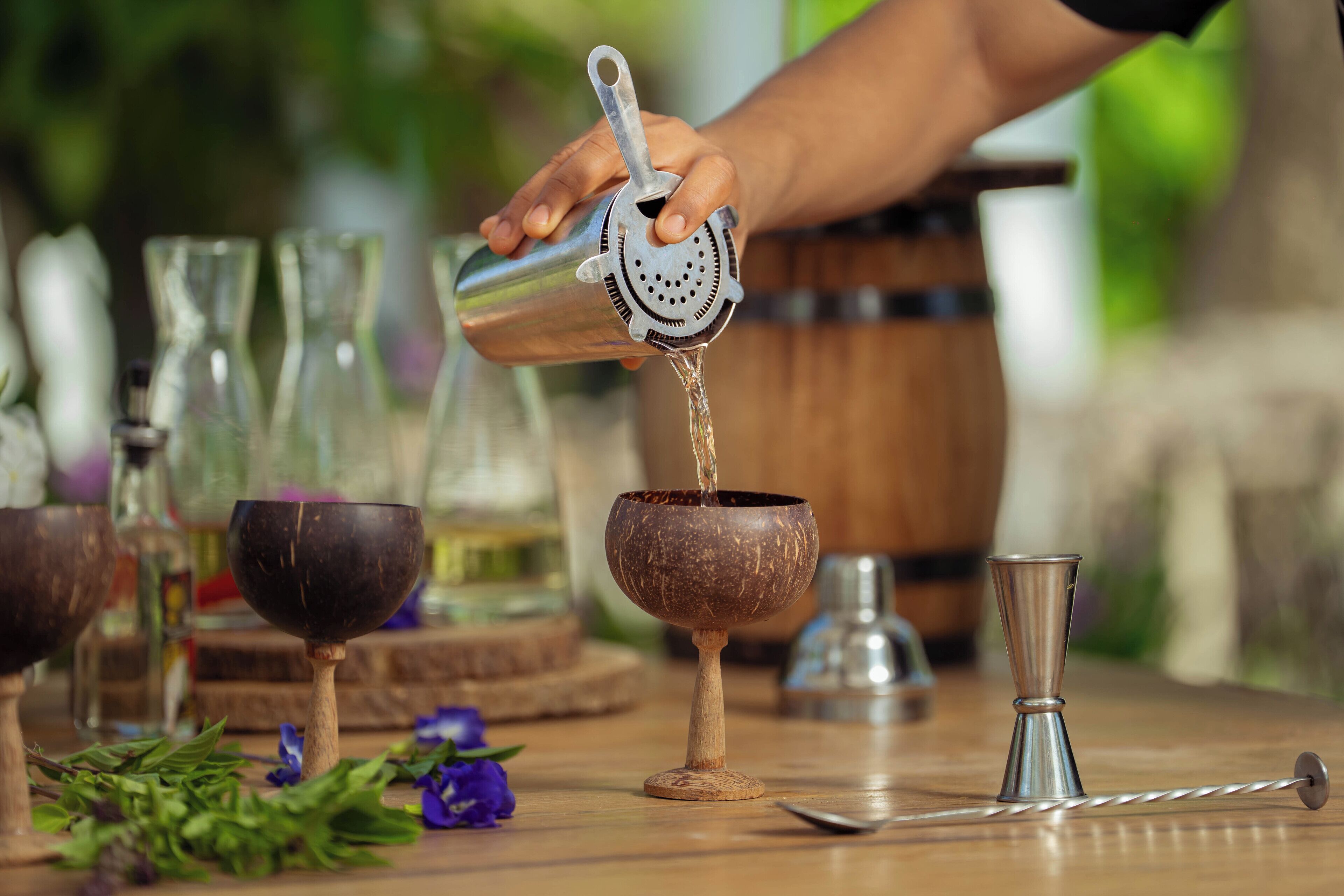 Une personne verse un liquide d’un shaker en métal dans un verre au style rustique.