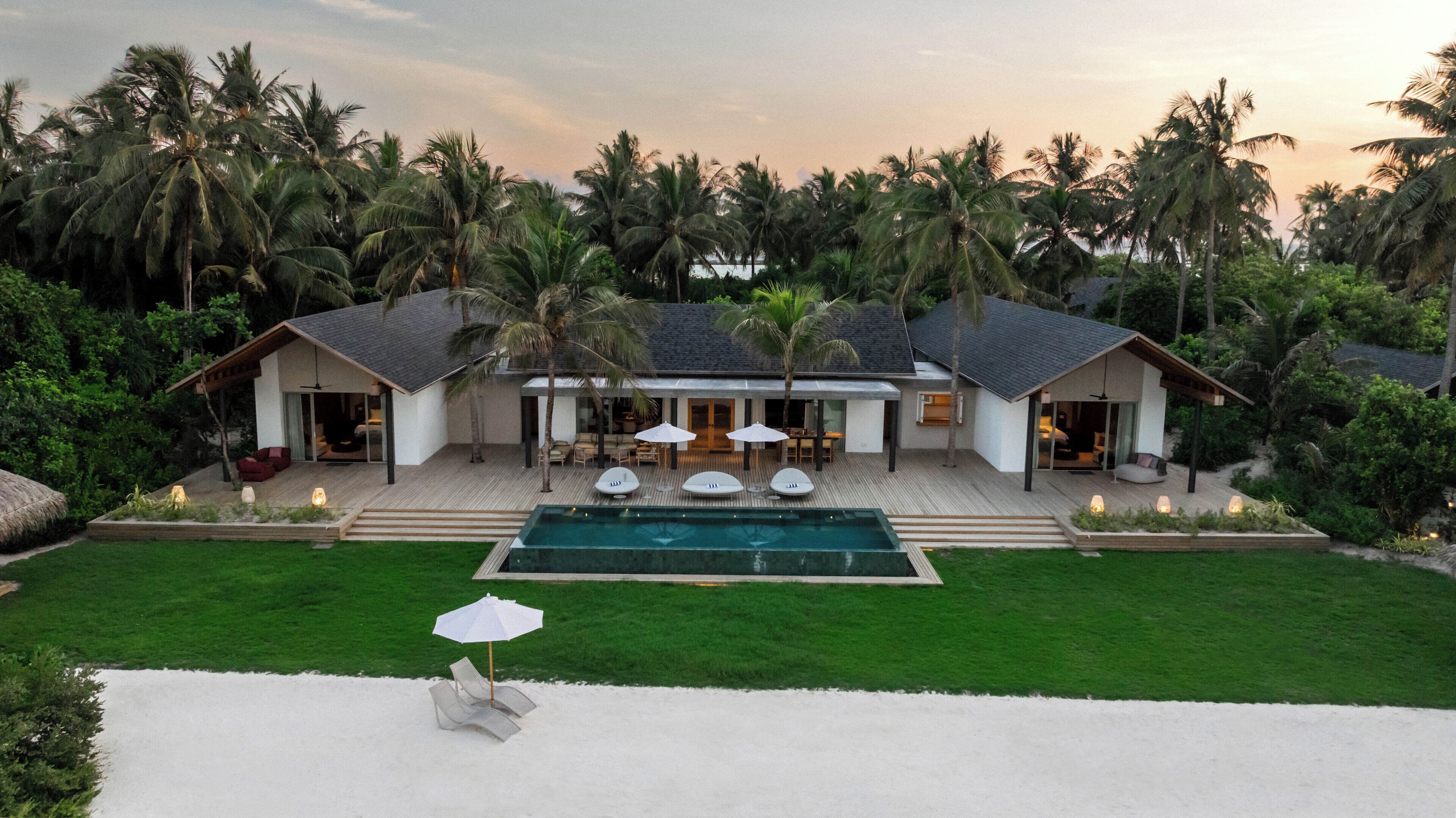 A modern house with a swimming pool, surrounded by palm trees and a well-maintained lawn.