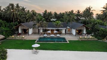 A modern house with a swimming pool, surrounded by palm trees and a well-maintained lawn.