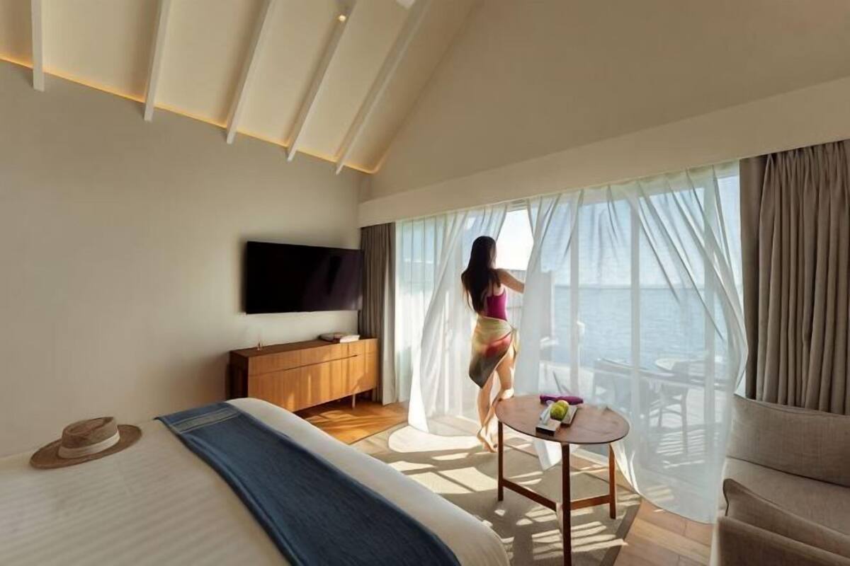 Ein Schlafzimmer mit Bett, Fernseher, einem Holzschrank, einem kleinen Tisch und Meerblick durch große Fenster.