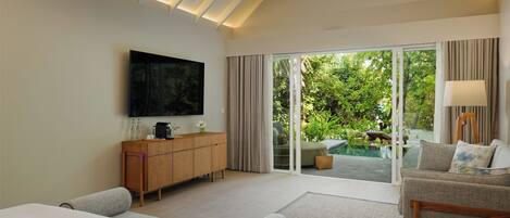 A modern hotel room with a large bed, a sofa, a TV, a wooden cabinet, and a sliding glass door leading to a pool area.