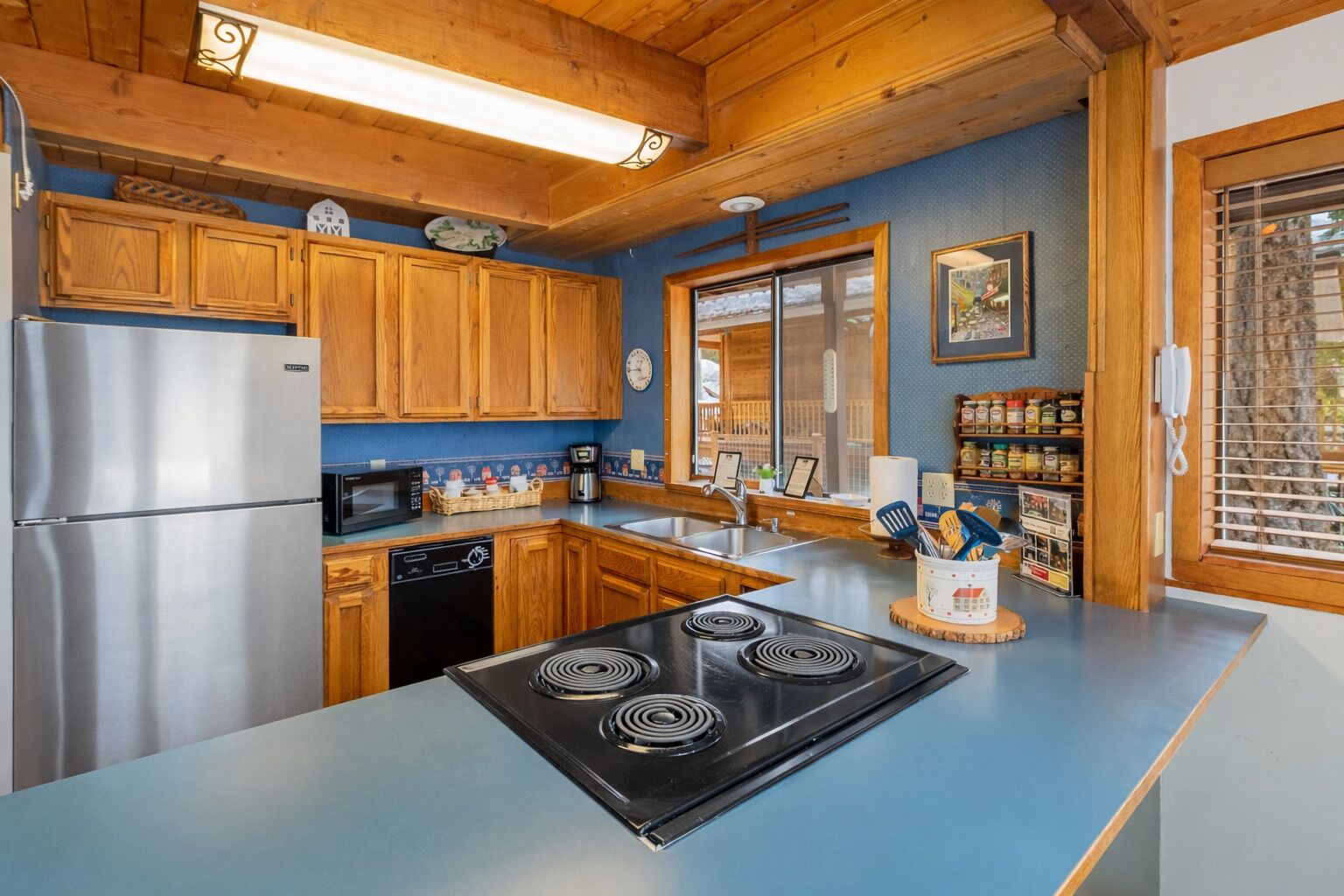 A modern kitchen with wooden cabinets, a stainless steel refrigerator, a black stove, and a blue countertop.