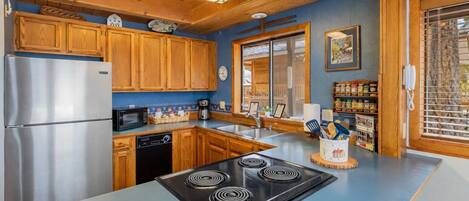 A modern kitchen with wooden cabinets, a stainless steel refrigerator, a black stove, and a blue countertop.