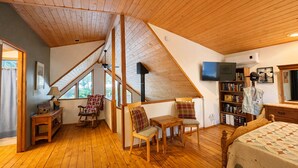 A cozy attic bedroom with wooden floors, a sloped ceiling, a bed, a TV, a bookshelf, and a window. - Jack's Cabin 2 Bedroom Home by NW Comfy Cabins (Leavenworth)