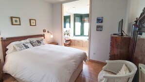 Une chambre avec un grand lit, une table de chevet, un bureau avec un ordinateur, une chaise et une vue sur une salle de bain avec une baignoire.