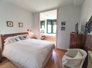 Un dormitorio con una cama grande, una mesita de noche, un escritorio con una computadora, una silla y vistas a un baño con bañera.