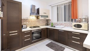 A modern kitchen with dark wooden cabinets, white countertops, a built-in oven, a microwave, and a window with vertical blinds. - Bluemarine Suite (St. Julian's)