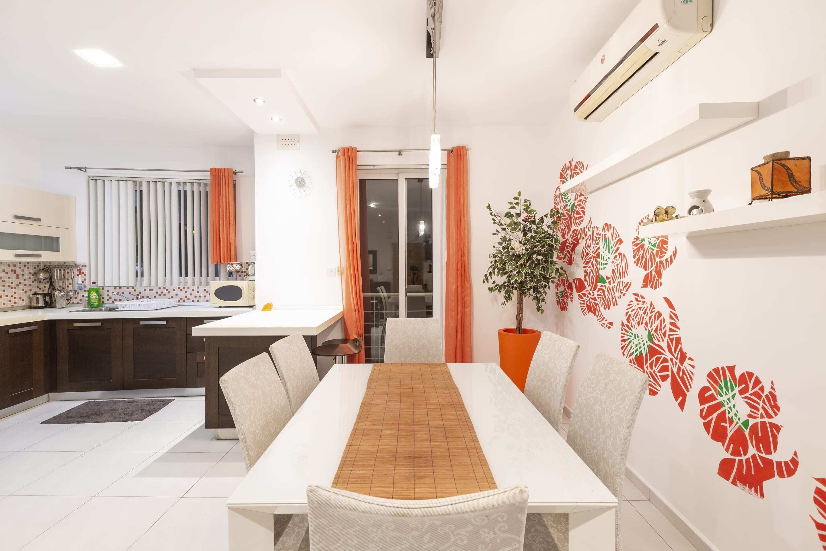 A modern kitchen with white cabinets, a microwave, and a dining area with a white table and chairs.