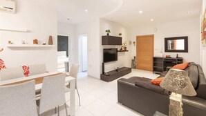 A modern living room with a sofa, TV, and dining area. - Bluemarine Suite (St. Julian's)