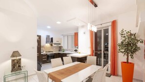 A modern dining area with a white table, cushioned chairs, and a central light fixture. - Bluemarine Suite (St. Julian's)