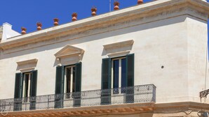 A building with three windows with green shutters, a balcony with a wrought iron railing, and terracotta pots on the roof. - Palazzo Acquaviva - Il Forno Antico (Lecce)